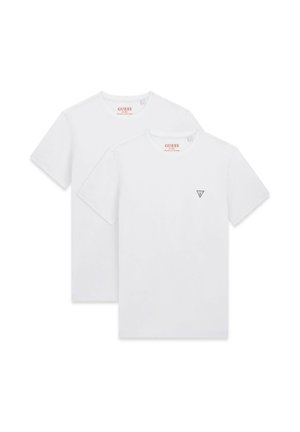 Due semplici t-shirt bianche a maniche corte, una leggermente dietro l'altra, entrambe con un piccolo logo triangolare Guess sul petto.