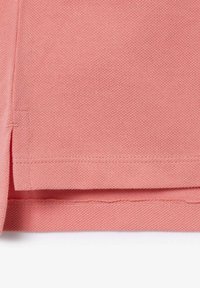 Tissu rose avec une surface texturée, soigneusement plié le long de l'ourlet, présentant une couture au bord et une légère finition brute d'un côté.