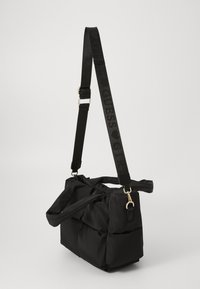 Black nylon handbag with quilted texture and a soft shape. Features a detachable strap with "GUESS" branding and gold-tone hardware accents.