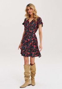 Černé květinové šaty s červenými a zelenými květy, volánkovými rukávy a mašlí v pase. Nosené s béžovými vysokými botami v uvolněném stylu.