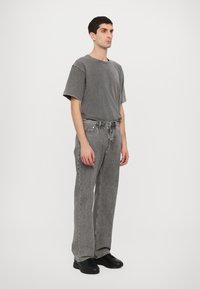 Gray cotton t-shirt with a relaxed fit, paired with gray denim pants featuring a loose cut and subtle texture, complemented by black sneakers.
