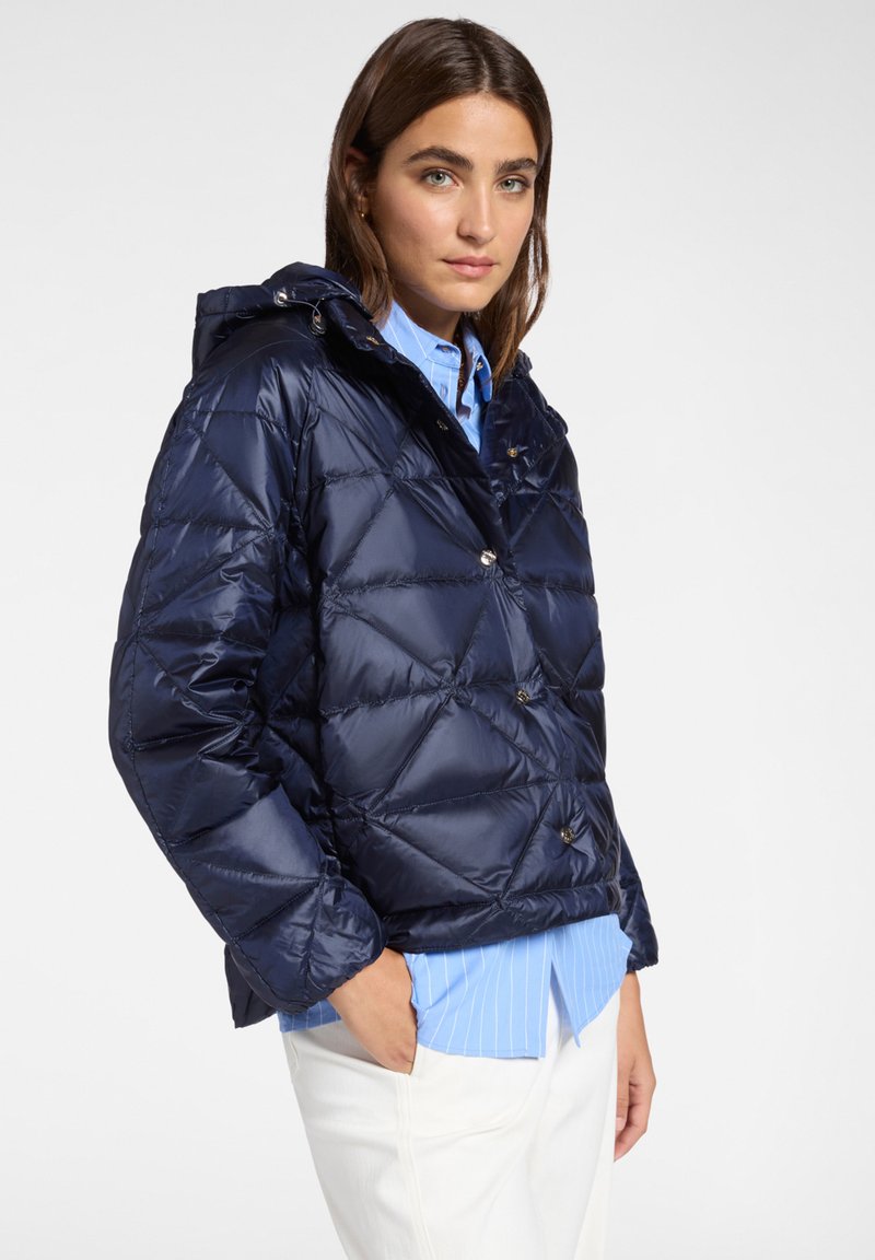 Granatowa kurtka puchowa z kapturem, prezentująca wzór w romby, kontrastujące srebrne guziki oraz błyszczące wykończenie. Pod spodem widoczna jest jasnoniebieska koszula.