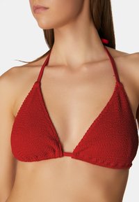 Roter dreieckiger Bikini-Oberteil aus strukturiertem Stoff, mit dünnen Trägern und einer Mittelbindeschnur. Auffälliges Detail ist ein subtil gerunzelt wirkendes Muster auf der Oberfläche.