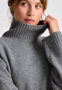 Suéter gris de cuello alto acanalado con un ajuste relajado y textura suave, que presenta un cuello alto y mangas largas y sueltas.