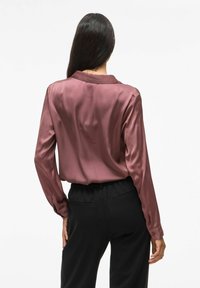 Camicia satinata a maniche lunghe di color malva con colletto, caratterizzata da una texture liscia. Abbinata a pantaloni neri, con vita elastica e tasche.