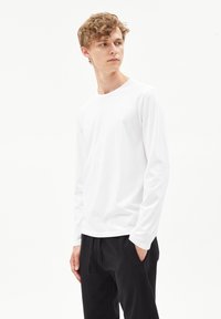 Witte lange mouwen t-shirt van zachte stof, met een ronde hals en een losse pasvorm, gecombineerd met zwarte joggers met trekkoord.