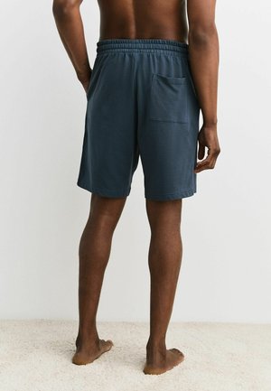 Marineblå shorts med elastisk taljebånd og baglomme. Fremstillet af letvægtsstof, med en afslappet pasform og længde over knæet.