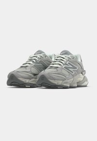 Ζευγάρι γκρι αθλητικών παπουτσιών New Balance 9060 με χοντρές σόλες και άσπρα κορδόνια σε απλό λευκό φόντο.