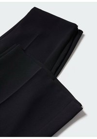 Pantalon formel noir plié avec des plis repassés visibles et une fermeture éclair sur un fond clair.