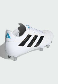 Hvid fodboldstøvle med sorte striber og gyldne syninger, med en afrundet tå, polstret krave og metalstød på sålen.