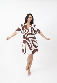 Braunes und weißes gemustertes Kleid mit tiefem V-Ausschnitt und kurzen, schwingenden Ärmeln, das eine fließende Silhouette und ein leichtes Material aufweist.