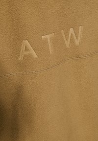 Beige fleece stof met een gladde textuur. Kenmerkt zich door verhoogde letters "ATW" en een zichtbare naaddetail. Geen extra patronen of accenten.