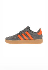 Gray suede sneaker with orange accents and three stripes, gum rubber sole, rounded toe, and lace-up design.