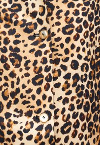 Ύφασμα με σχέδιο λεοπάρδαλης με καφέ και μαύρες κηλίδες σε μπεζ φόντο. Διαθέτει κυκλική κλείστρα με κουμπί. Απαλή υφή, casual σχεδιασμός.