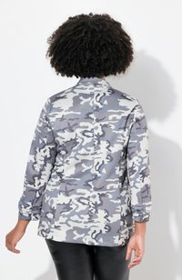 Giacca con motivo camouflage in grigio e bianco, maniche lunghe, colletto alto, texture liscia, con schiena dritta e dettagli di plissettatura discreti.