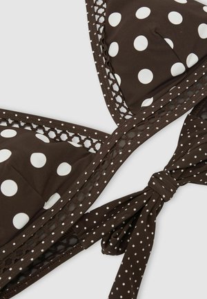 Brązowy top bikini z dużymi białymi groszkami, wykończeniem z siateczki oraz wiązaniem z małymi białymi groszkami na jednolitym tle.