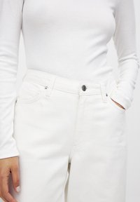 Witte ribboord lange mouwen top gecombineerd met hooggesneden witte jeans met knoopsluiting en voorzakken. Glad denim textuur.