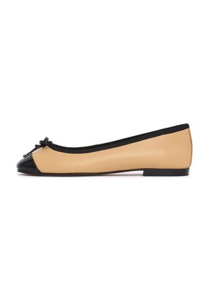 Zapato plano de ballet beige con puntera negra, ribete negro, pequeño lazo en la parte delantera y suela plana negra, mostrado de perfil sobre fondo blanco.