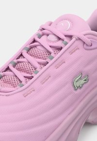 Chaussure de sport rose avec dessus en mesh, lacets croisés avec accents réfléchissants, et logo crocodile argenté sur le panneau latéral.