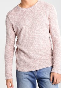 Ljusrosa långärmad skjorta med ett strukturerat stickat mönster, rund halsringning och en avslappnad passform, tillsammans med blå jeans.