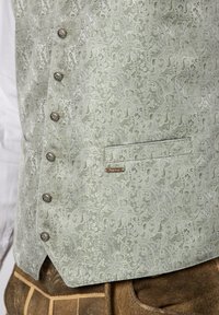 Hellgrüne Weste mit Paisleymuster, metallischen Knöpfen und einer Tasche. Texturierter Stoff mit subtiler Glanz, der ein Markenschild zeigt.