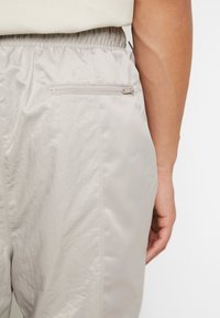 Hellbeige Hosen mit strukturiertem Finish, ausgestattet mit einem elastischen Bund und einer Reißverschluss-Rückentasche für sichere Aufbewahrung.