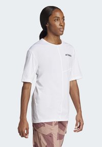 Bílý tričko s krátkým rukávem a kulatým výstřihem, s kontrastním prošitím a černým logem "TERREX" na hrudi.