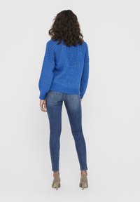 Blue knitted sweater with textured pattern on the back, paired with slim-fit denim jeans and beige high-heeled shoes.