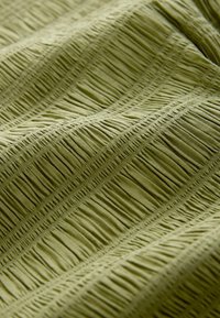 Oliivinvihreä, teksturoitu kangas, jossa on pystysuoria laskoksia ja sileä pinta, tasaisesti sijoitetuilla uurteilla, jotka luovat syvyyttä ja kuvion.