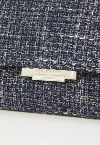 Marineblaue strukturierte Stofftasche mit silbernen Beschlägen. Mit einem Logo-Schild, gewebtem Design und einer Klappenöffnung. Glattes Innenfutter.