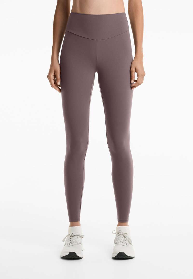 Leggings visokog struka u mekom mauve tkanju s glatkom teksturom i minimalnim šavovima, uparenim s bijelim sportskim cipelama.