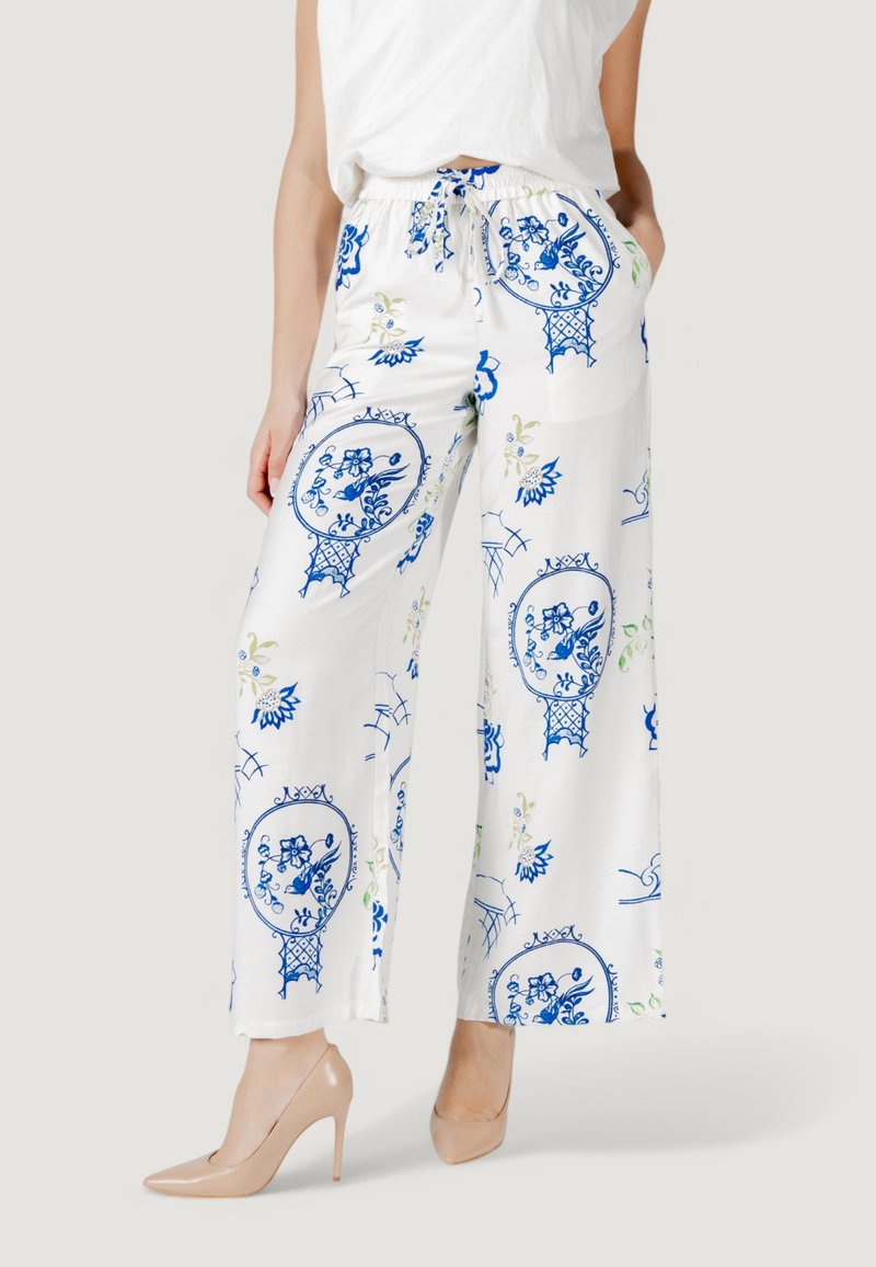 Pantaloni bianchi a gamba larga con motivi floreali blu, vita con cordino e tasche. Abbinati a scarpe con tacco nude.