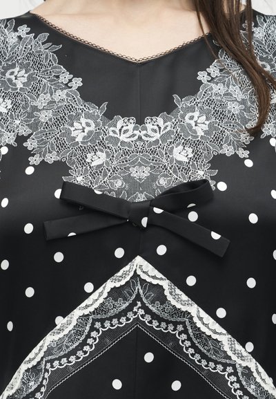 Μαύρο τοπ με λευκά πουά, λευκή δαντέλα με λουλούδια γύρω από τη γραμμή του λαιμού και το στήθος, και μαύρη κορδέλα δεμένη στο κέντρο.