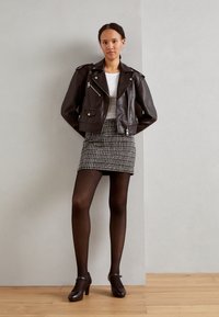 Brun skinnjakke for motorsykkel over en hvit topp, kombinert med et svart-hvitt mønstret miniskjørt og sorte leggings. Brune høyhælte sko.