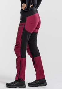 Waterproof pants with a black and maroon color scheme, featuring zippered pockets, reinforced knees, and an adjustable waistband for fit.