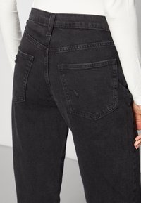 Svarta denimjeans med hög midja, utrustade med två bakfickor och en lätt sliten detalj. Mjukt material med minimal sömnad.