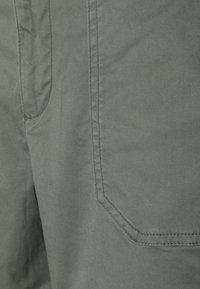 Tejido de algodón gris con textura suave, que presenta un bolsillo y detalles de costura. La tela tiene un brillo sutil y un diseño discreto.