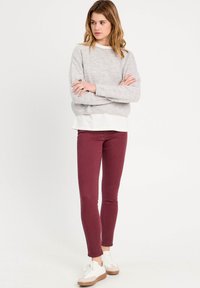 Sweatshirt en tricot gris avec un col large, superposé sur une chemise blanche. Leggings bordeaux et baskets blanches à semelles beige. Look décontracté.