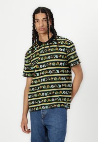 Svart t-skjorte med korte ermer som har fargerike vertikale mønstre av planter, stjerner og tall på en horisontal stripe design.