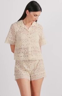 Kanten pyjama set in lichtbeige met korte mouwen, een knoopsluiting aan de voorkant en bijpassende shorts met een bloemenpatroon en golvende randen.