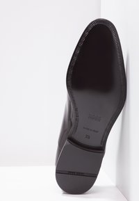 Semelle de chaussure en cuir noir avec une finition lisse, une forme arrondie et des accents en caoutchouc. Les marquages incluent le nom de la marque et les détails de taille. Fabriqué en Italie.