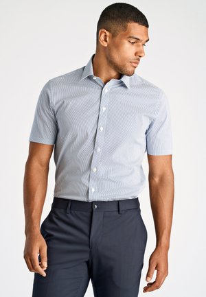 Korte mouwen overhemd met knopen in lichtblauw met een klein wit geometrisch patroon; gecombineerd met donkerblauwe broek, gladde stof. 