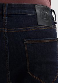 Mörkblå denimjeans med orange sömnad, med en läderetikett med "CR7"-logotyp. Inkluderar bakfickor och en stilren design.