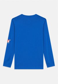 Hosszú ujjú póló élénk kék pamutból. Kerek nyakkivágással és mandzsettával rendelkezik, a bal ujján pedig egy kis logó található.