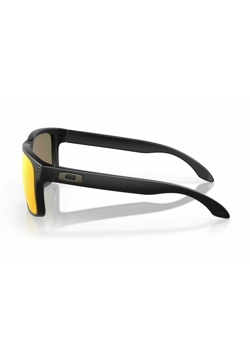 Lunettes de soleil noires avec des verres jaunes plats, dotées d'une monture en plastique robuste et de branches courbées élégantes. Comprend des accents métalliques sur la branche.