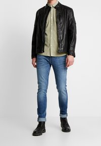 Svart läderjacka, olivgrön knäppskjorta, ljusblå jeans, uppvikta ärmar och svarta snörskor. Har minimal hårdvarudetaljer.