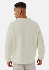 Weißer Fleece-Pullover mit lässiger Passform, langen Ärmeln und rundem Ausschnitt. Weiche Textur und leicht übergrößeres Design.