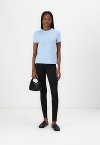 T-shirt bleu clair à manches courtes avec une coupe classique, associé à des leggings noirs et un sac noir. Texture en coton lisse et design simple.