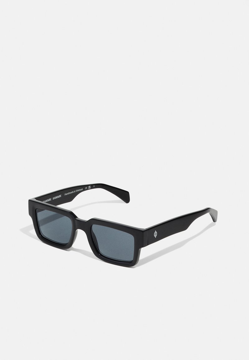 Black rectangular sunglasses with a matte finish, dark tinted lenses, and subtle logo detail on the side of the frame. Unique angular design.