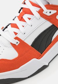 Valkoinen nahkainen lenkkari mustilla yksityiskohdilla, oransseilla mokkanahkadetaljeilla ja valkoisella verkkokielekkeellä. Varustettu valkoisilla nauhoilla ja kuvioidulla pohjalla.